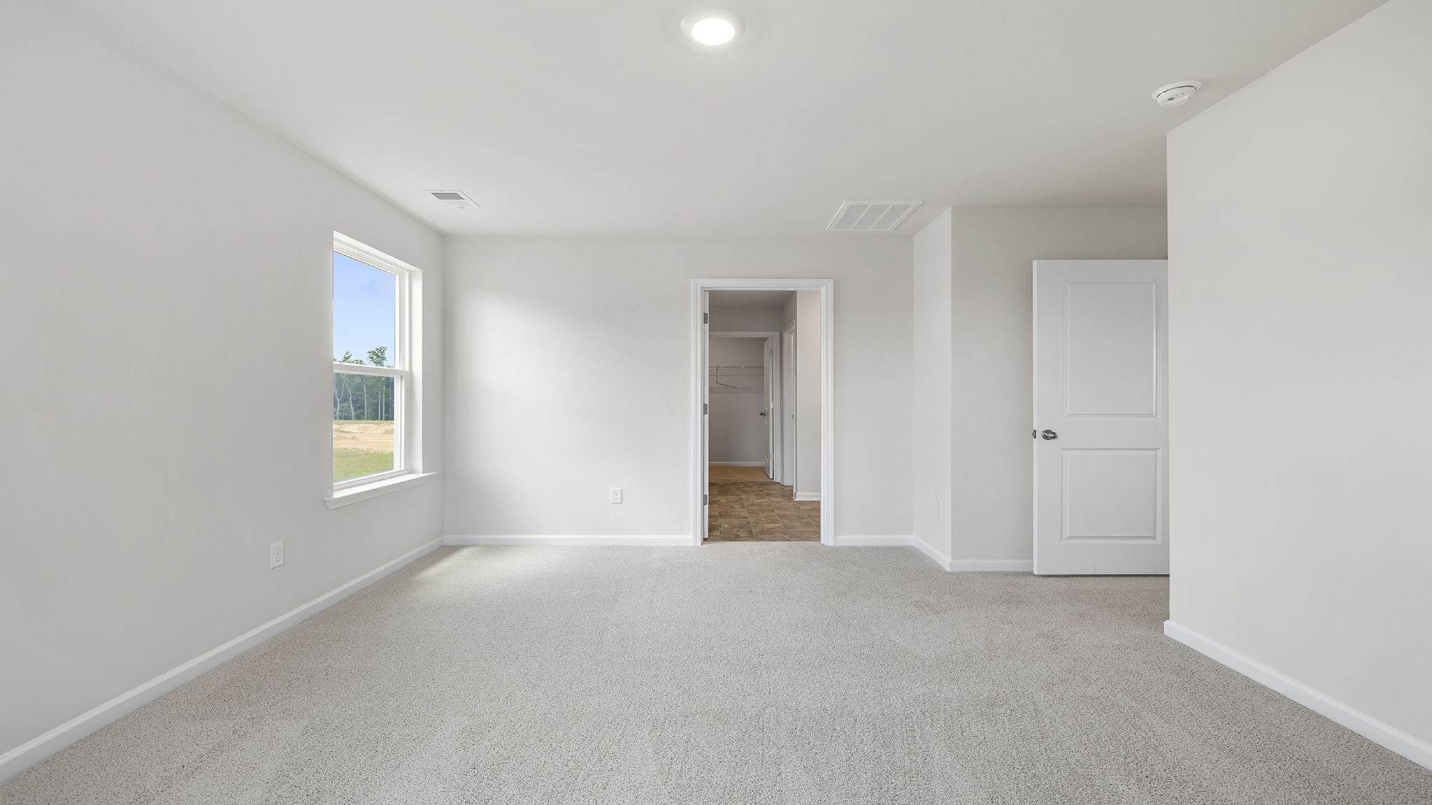 Primary bedroom with carpet and window.