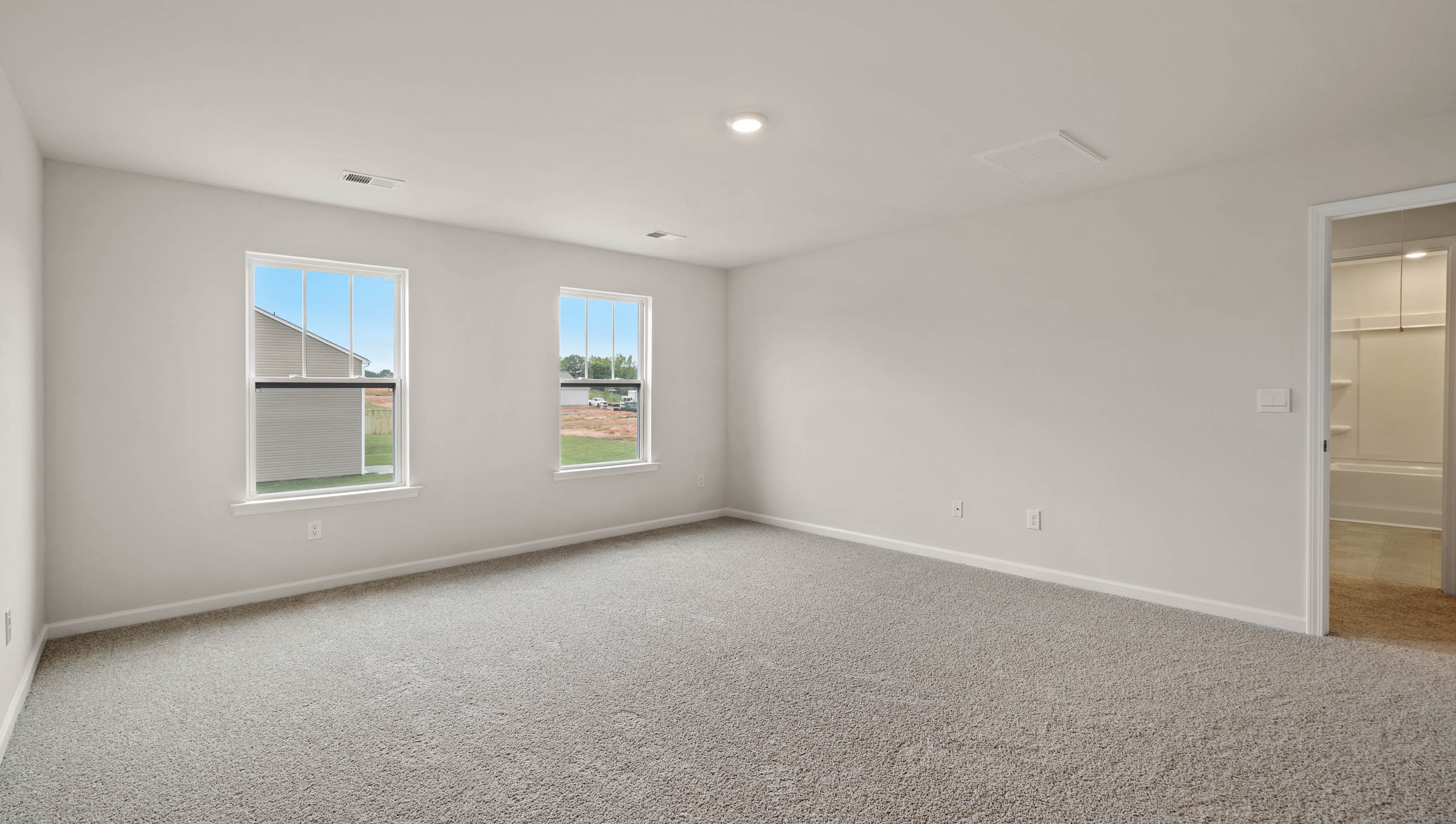 Primary bedroom with two large windows and carpet.