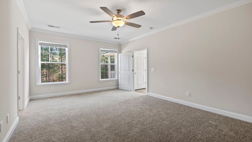Primary bedroom with windows, ceiling fan and carpet.