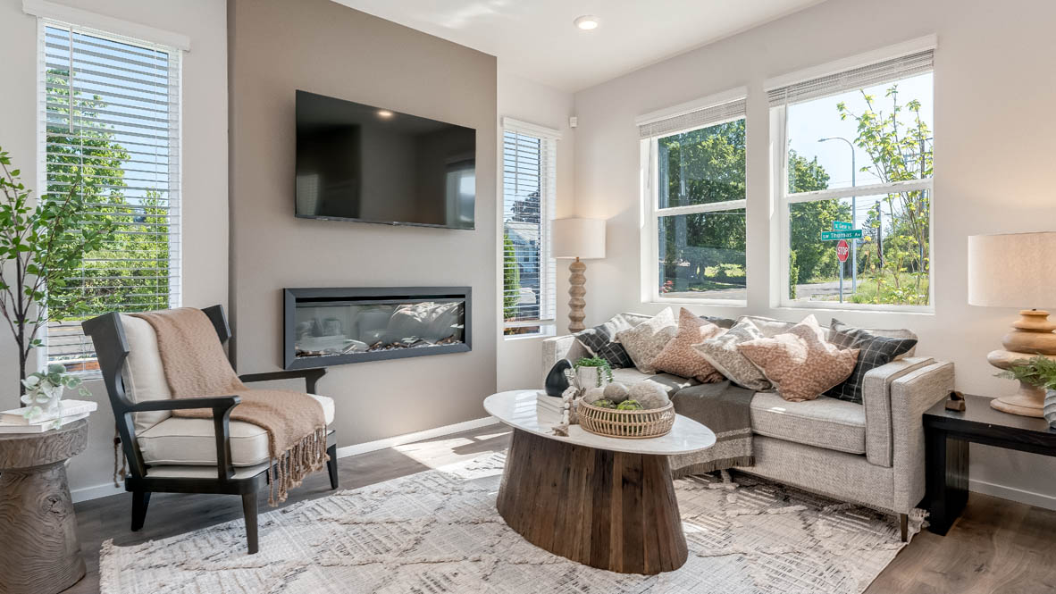 Terrace at Pleasant Valley Great room with a white couch and pillows, electric fireplace, chair, white rug, wood coffee table, laminate flooring, a lamp, and windows