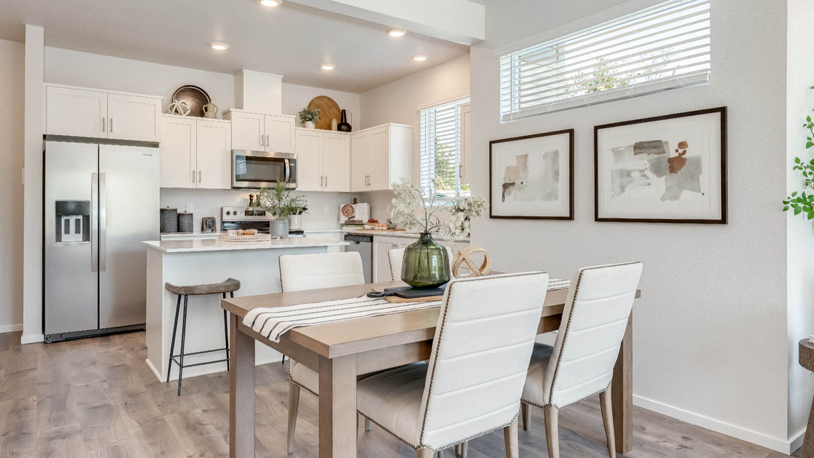 Terrace at Pleasant Valley Dining and Kitchen with a table with four white chairs, laminate flooring, two paintings, a long window, and the kitchen in the background