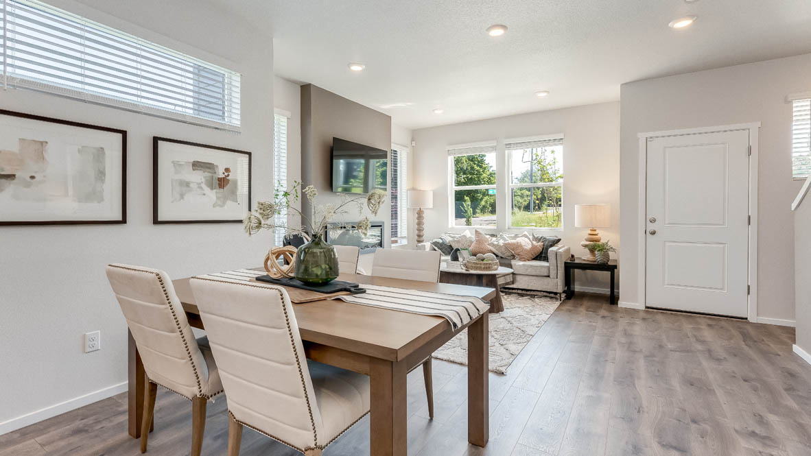Terrace at Pleasant Valley Dining and Great room with a table with four white chairs, laminate flooring, two paintings, a long window, and the great room in the background