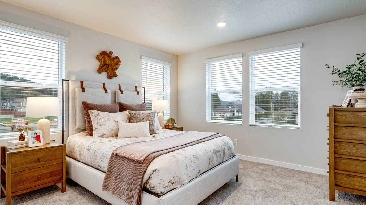 Butler Creek Crossing Primary bedroom with white carpet, hanging paintings, two side tables, two lamps, a chair, windows with curtains