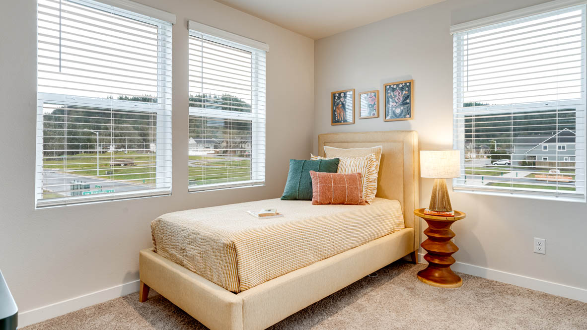 Butler Creek Crossing bedroom with side table and a lamp, bed, paintings, desk with a chair, and window with shades