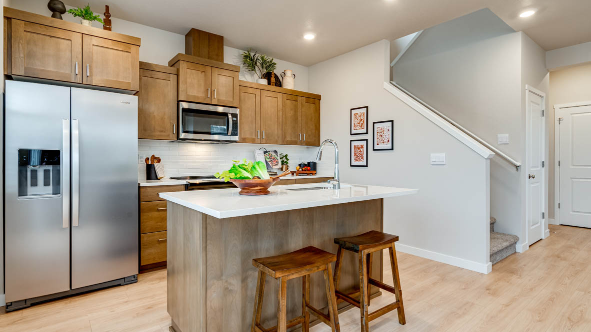 Butler Creek Crossing Kitchen with island that has white quartz countertops, two seats set up at the island, stainless steel appliances, a sliding glass door to the backyard, and stained shaker style cabinets