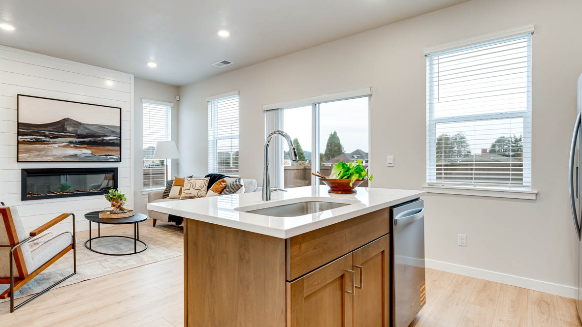 Butler Creek Crossing Kitchen with island that has white quartz countertops, two seats set up at the island, stainless steel appliances, a sliding glass door to the backyard, and stained shaker style cabinets