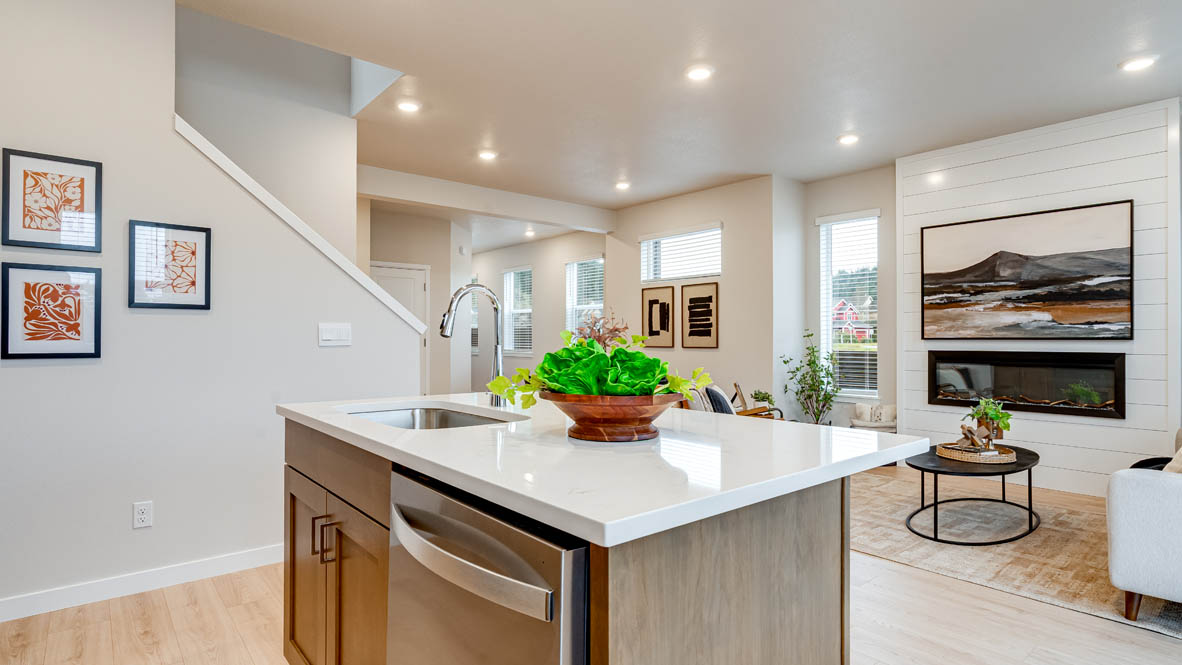 Butler Creek Crossing Kitchen with island that has white quartz countertops, two seats set up at the island, stainless steel appliances, a sliding glass door to the backyard, and stained shaker style cabinets