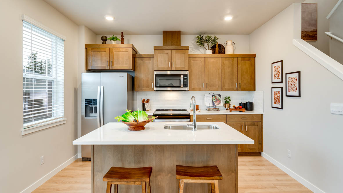 Butler Creek Crossing Kitchen with island that has white quartz countertops, two seats set up at the island, stainless steel appliances, a sliding glass door to the backyard, and stained shaker style cabinets