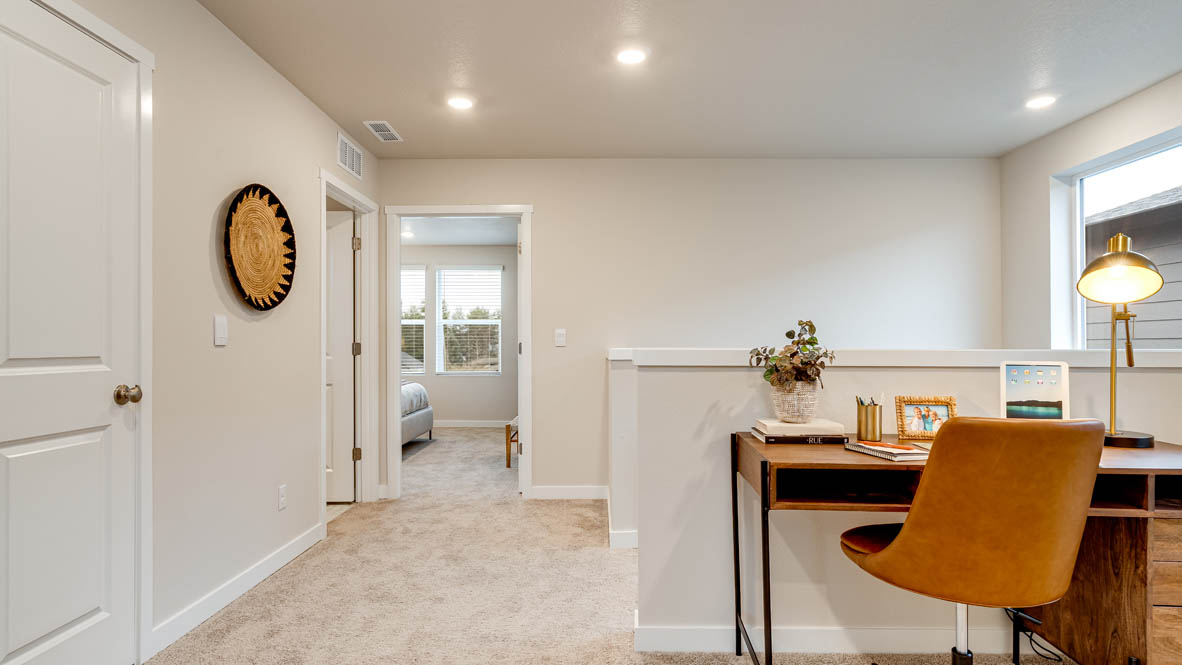 Butler Creek Crossing Loft with carpet, hallway, a decorative hanging art piece, a desk with a burnt orange chair, and windows