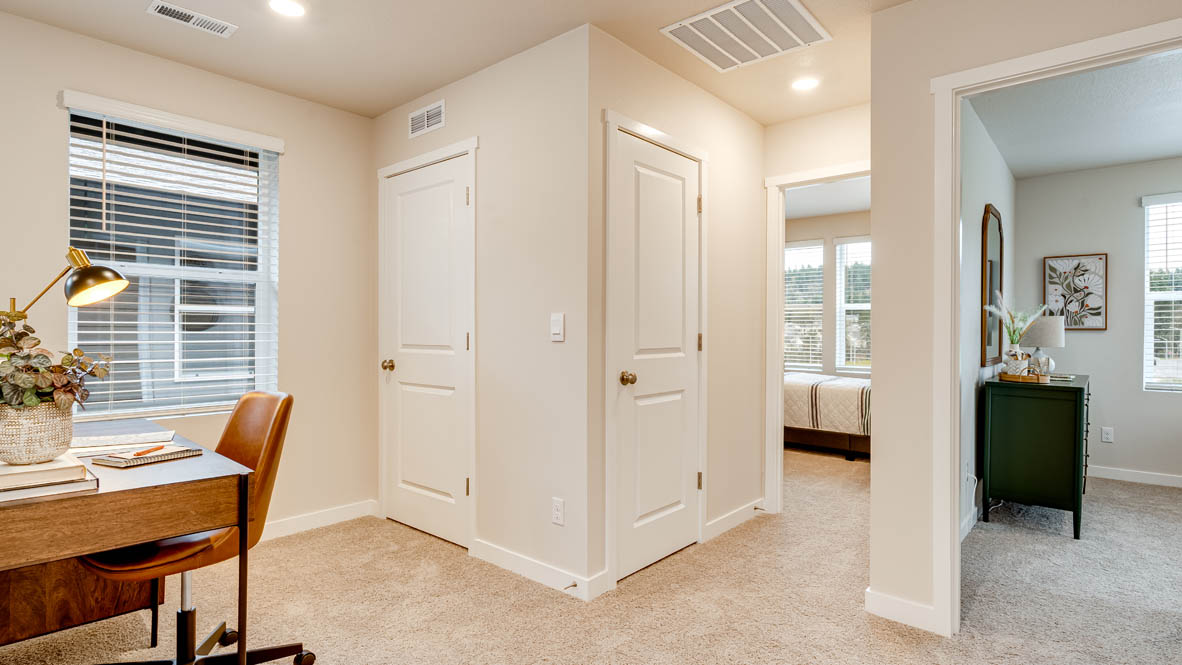 Butler Creek Crossing Loft with carpet, hallway, a decorative hanging art piece, a desk with a burnt orange chair, and windows