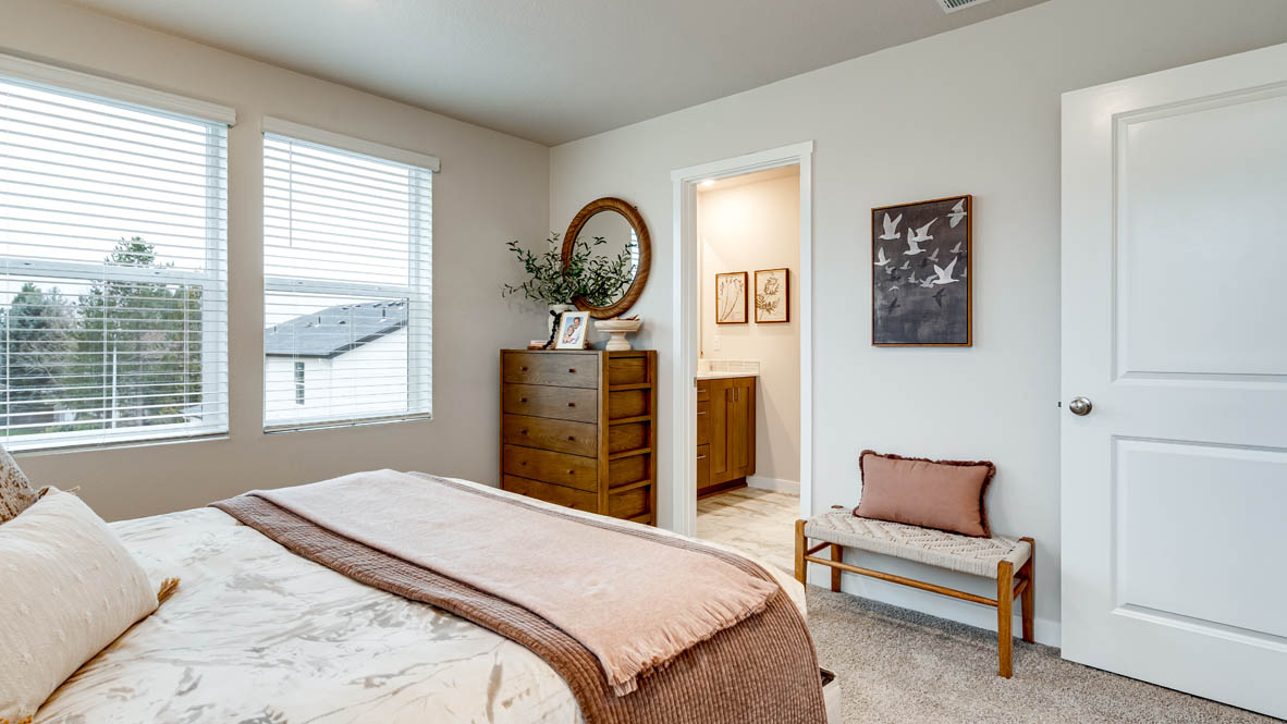 Butler Creek Crossing Primary bedroom with white carpet, hanging paintings, two side tables, two lamps, a seat, windows with curtains