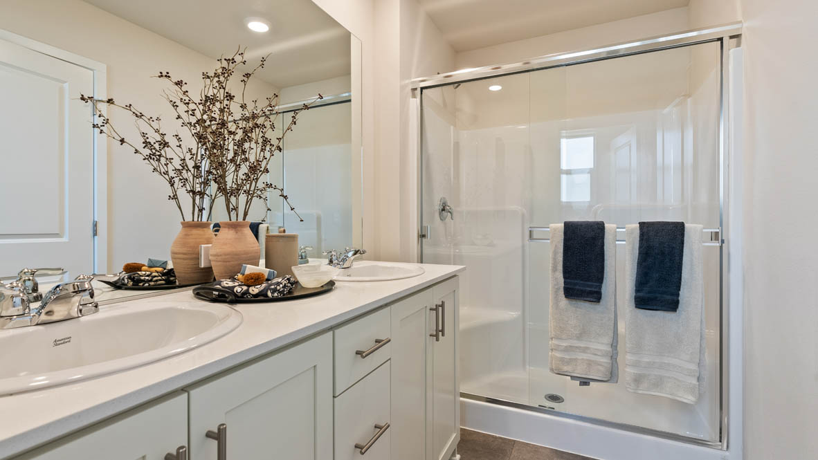 Butler Creek Crossing primary bathroom with double vanity, mirror, decor plant, walk in shower with sliding glass door