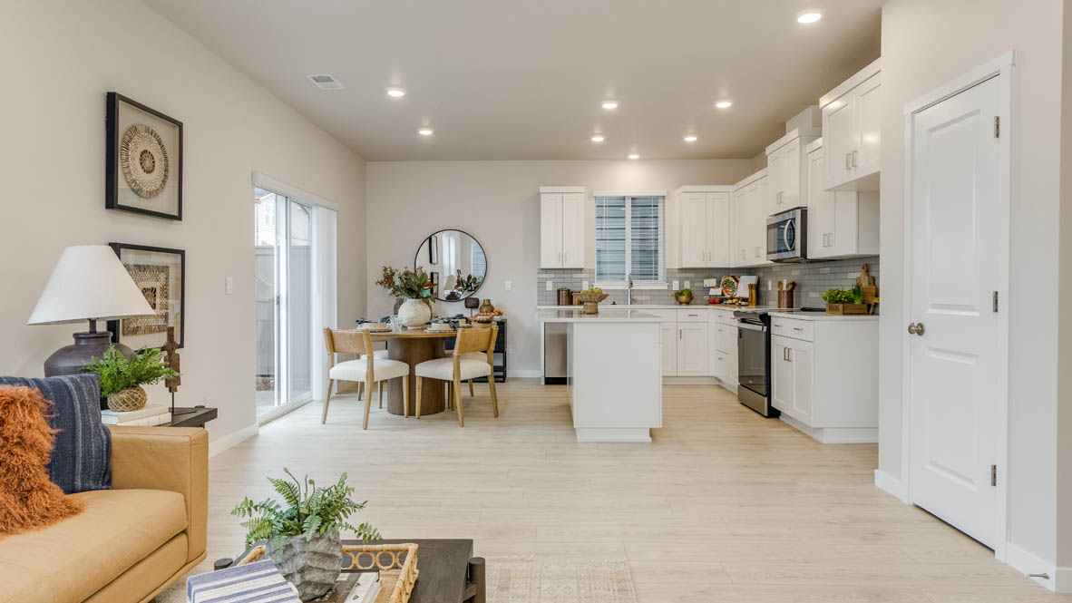 Butler Creek Crossing Kitchen with island that has white quartz countertops, two seats set up at the island, stainless steel appliances, a sliding glass door to the backyard, and stained shaker style cabinets