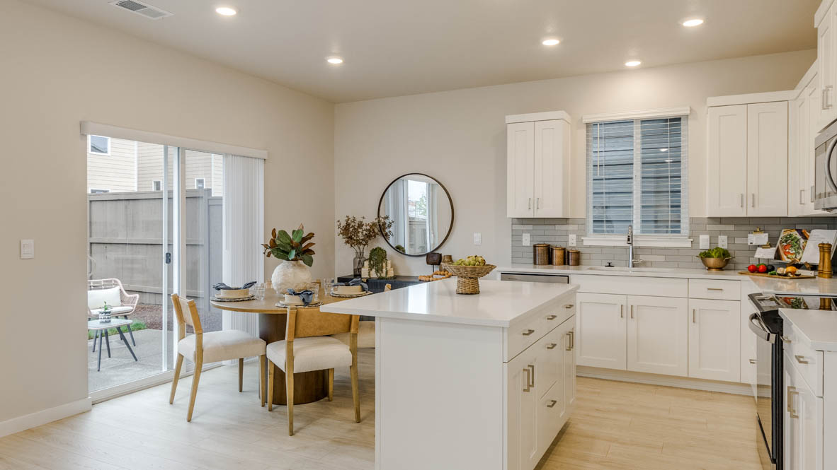 Butler Creek Crossing Kitchen with island that has white quartz countertops, two seats set up at the island, stainless steel appliances, a sliding glass door to the backyard, and stained shaker style cabinets