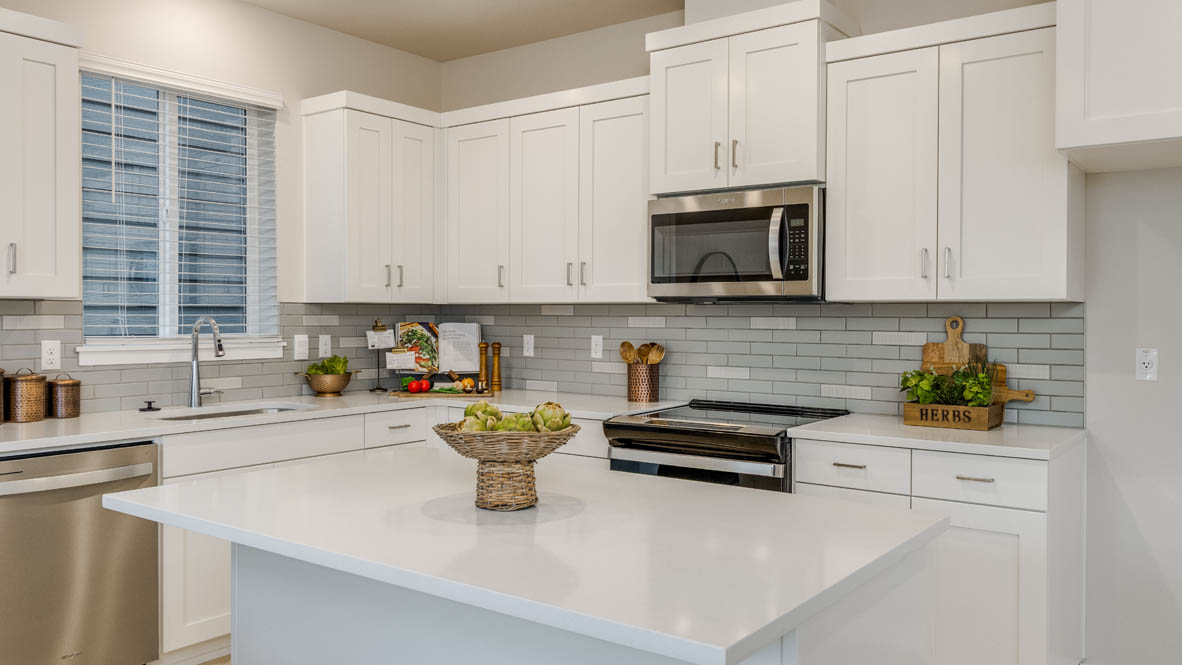 Butler Creek Crossing Kitchen with island that has white quartz countertops, two seats set up at the island, stainless steel appliances, a sliding glass door to the backyard, and stained shaker style cabinets