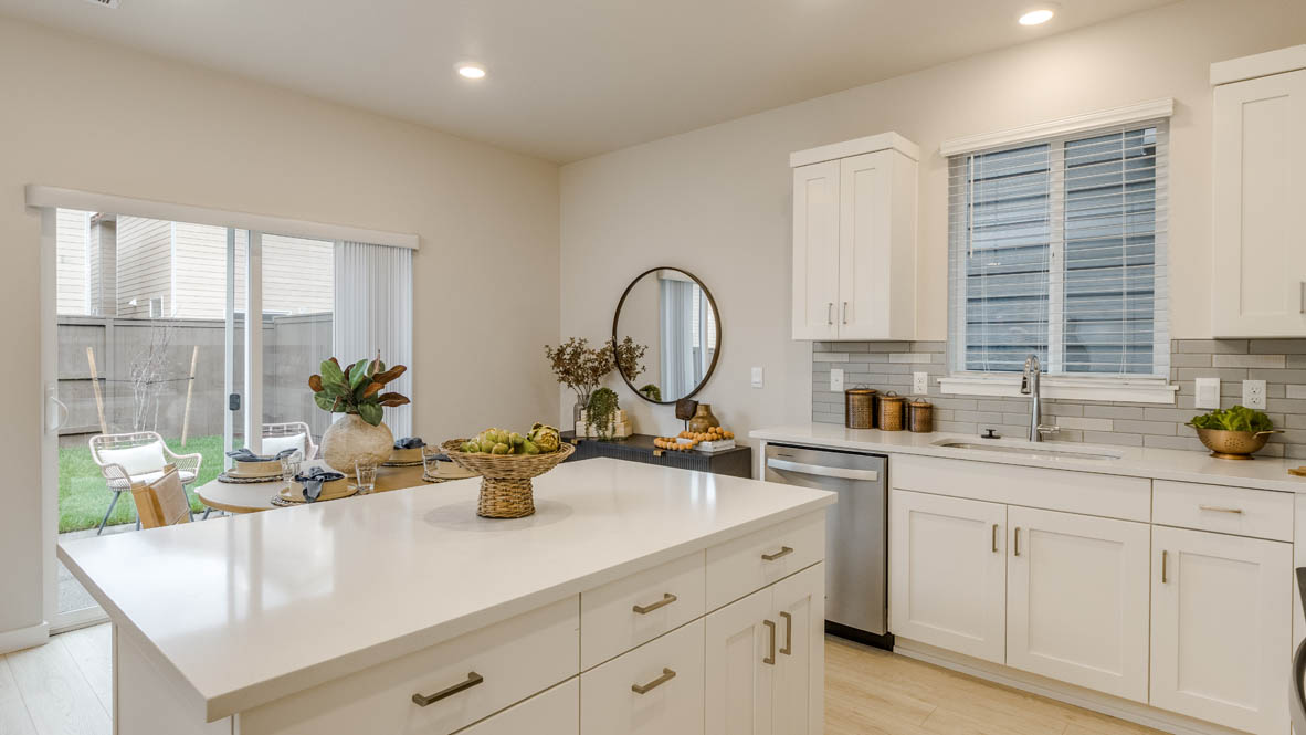 Butler Creek Crossing Kitchen with island that has white quartz countertops, two seats set up at the island, stainless steel appliances, a sliding glass door to the backyard, and stained shaker style cabinets
