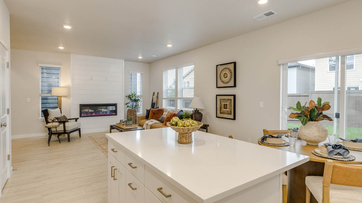 Butler Creek Crossing Kitchen with island that has white quartz countertops, two seats set up at the island, stainless steel appliances, a sliding glass door to the backyard, and stained shaker style cabinets