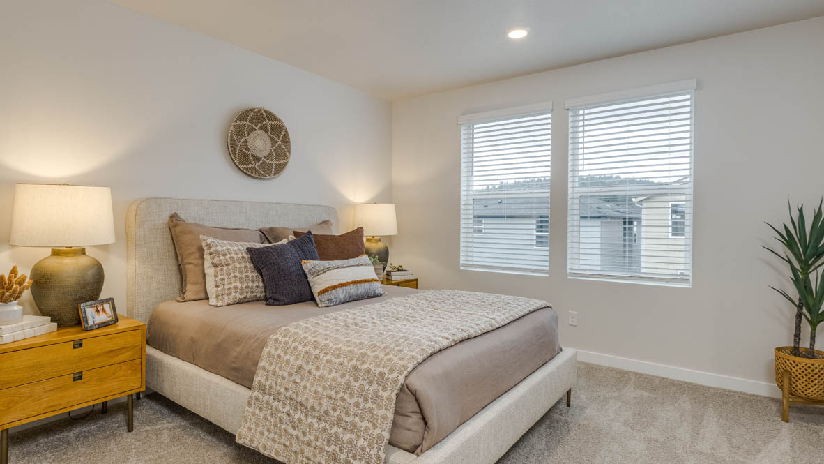 Butler Creek Crossing Primary bedroom with white carpet, hanging paintings, two side tables, two lamps, a chair, windows with curtains