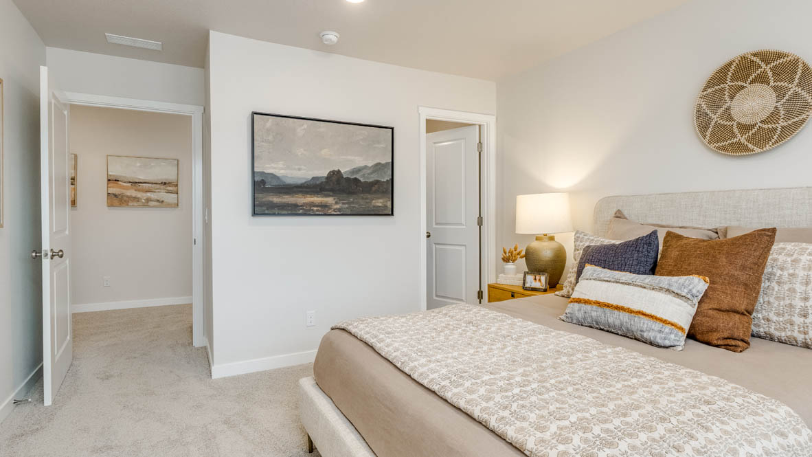 Butler Creek Crossing Primary bedroom with white carpet, hanging paintings, two side tables, two lamps, a seat, windows with curtains