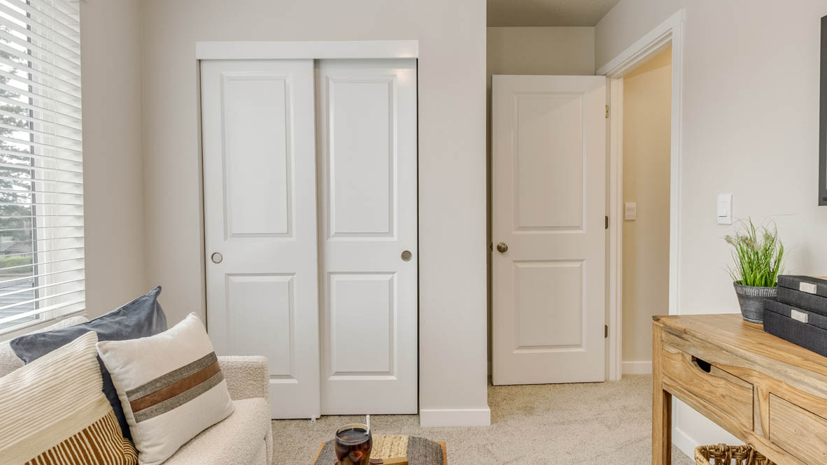 Butler Creek Crossing bedroom with side table and a lamp, bed, paintings, desk with a chair, and window with shades, and a closet
