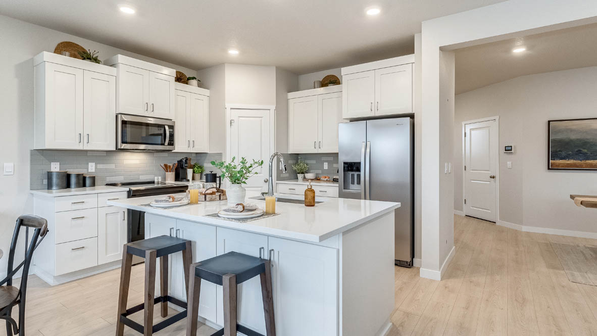 Butler Creek Crossing Kitchen with island that has white quartz countertops, two seats set up at the island, stainless steel appliances, a sliding glass door to the backyard, and white shaker style cabinets