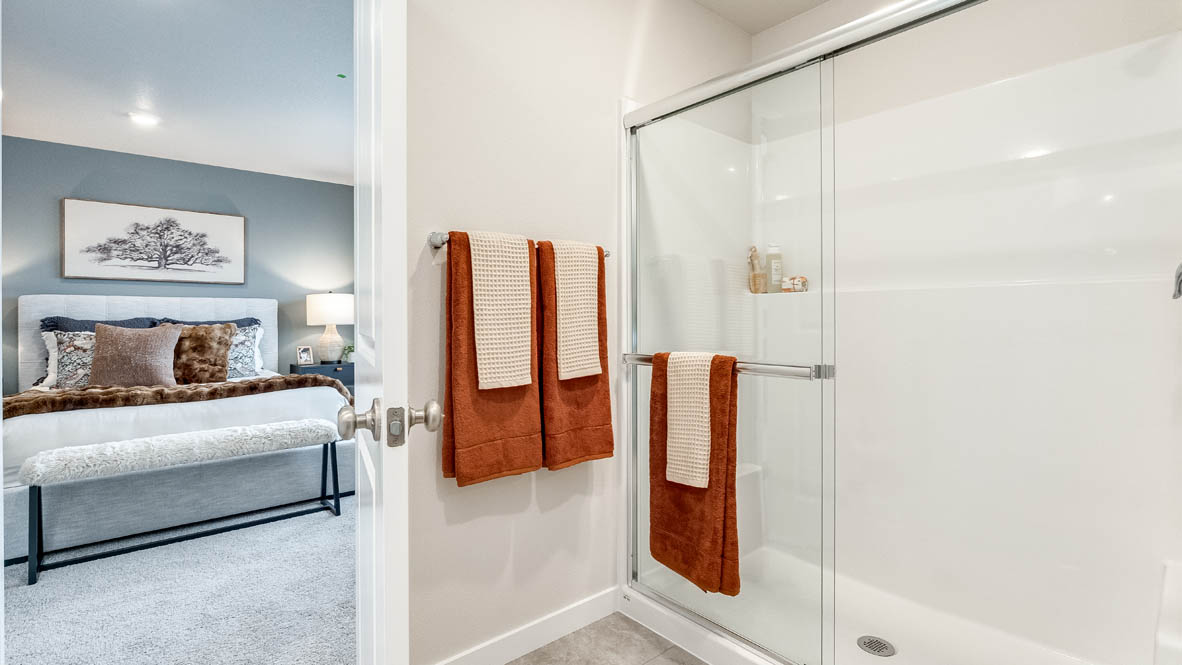 Butler Creek Crossing primary bathroom with a walk-in shower with sliding glass doors, and primary bedroom in the background