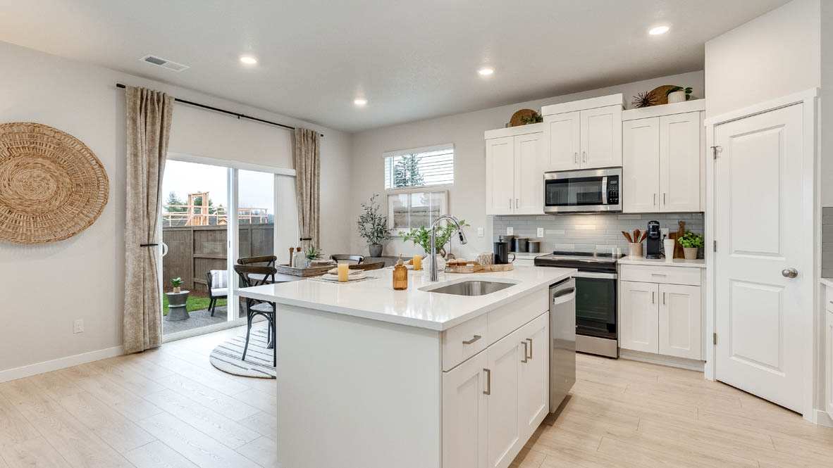 Butler Creek Crossing Kitchen with island that has white quartz countertops, two seats set up at the island, stainless steel appliances, a sliding glass door to the backyard, and white shaker style cabinets