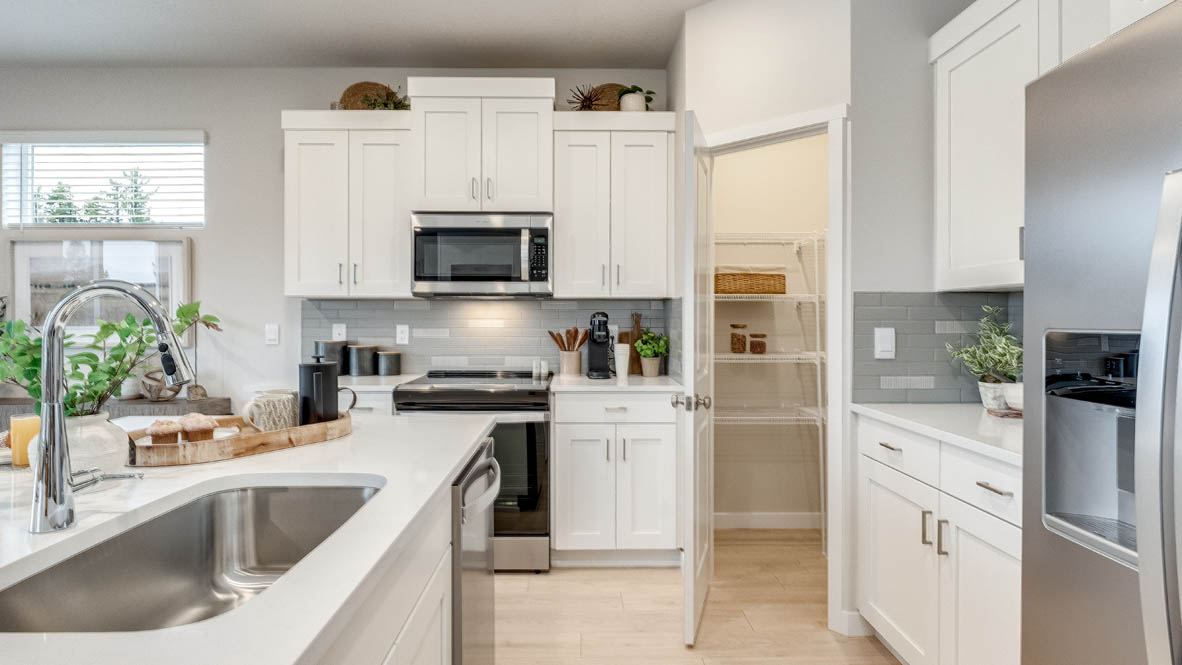 Butler Creek Crossing Kitchen with island that has white quartz countertops, two seats set up at the island, stainless steel appliances, a sliding glass door to the backyard, and white shaker style cabinets