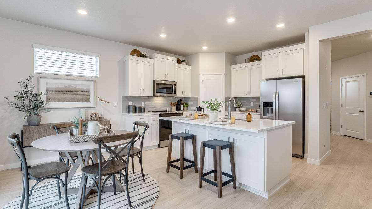 Butler Creek Crossing Kitchen with island that has white quartz countertops, two seats set up at the island, stainless steel appliances, a sliding glass door to the backyard, and white shaker style cabinets