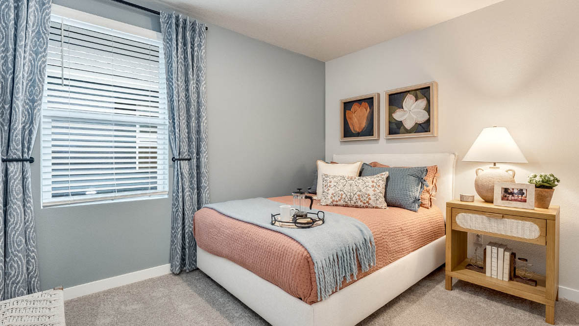 Butler Creek Crossing bedroom with side table and a lamp, bed, paintings, desk with a chair, and window with shades