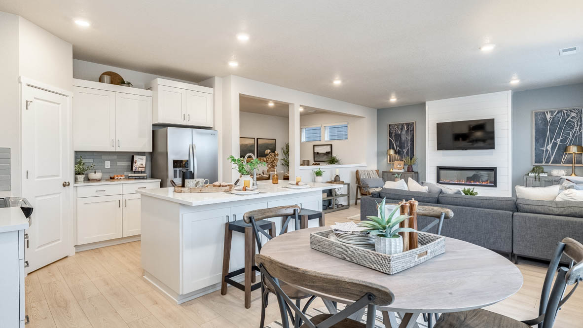 Butler Creek Crossing Kitchen and dining table with four chairs, with island that has white quartz countertops, two seats set up at the island, stainless steel appliances, and white shaker style cabinets