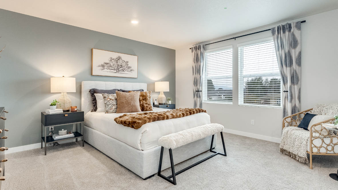 Butler Creek Crossing Primary bedroom with white carpet, three hanging paintings, two side tables, two lamps, a chair, windows with curtains