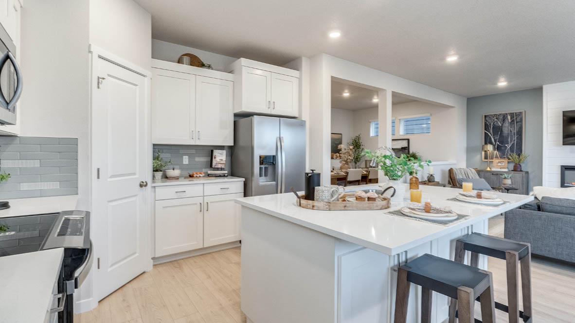 Butler Creek Crossing Kitchen with island that has white quartz countertops, two seats set up at the island, stainless steel appliances, a sliding glass door to the backyard, and white shaker style cabinets