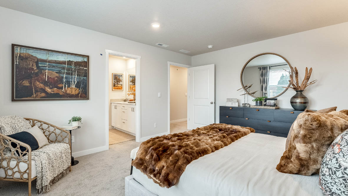 Butler Creek Crossing Primary bedroom with white carpet, three hanging paintings, two side tables, two lamps, a chair, windows with curtains