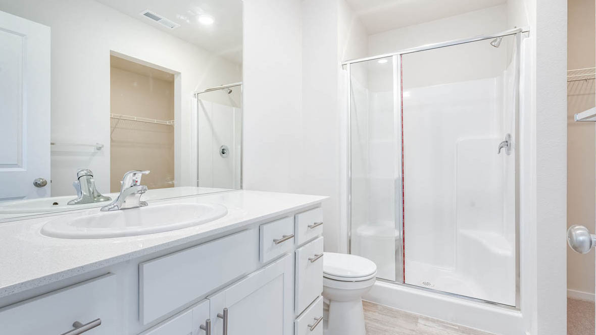 East Park Village primary bathroom with vanity, mirror, toilet, walk in shower, and white cabinets