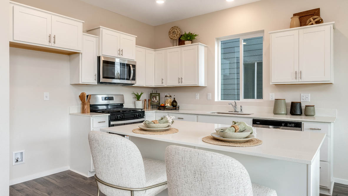 East Park Village Kitchen with island and a breakfast bar, two chairs, white cabinets, stainless steel appliances, quartz countertops, a window, decorations, and laminate flooring