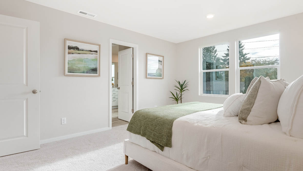 East Park Village Primary bedroom with carpet and a bed with a white bedframe, two end tables, two lamps, pillows, windows, and plants