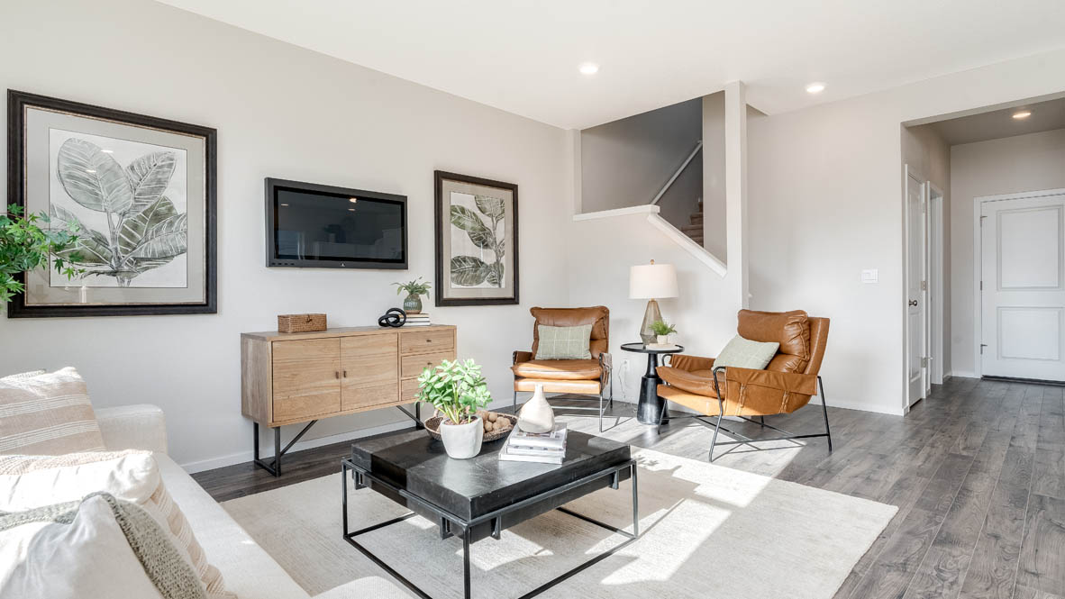 East Park Village great room with laminate flooring, white carpet, a brown chair, entertainment center, white couch, glass coffee table, plants, paintings, and a tv