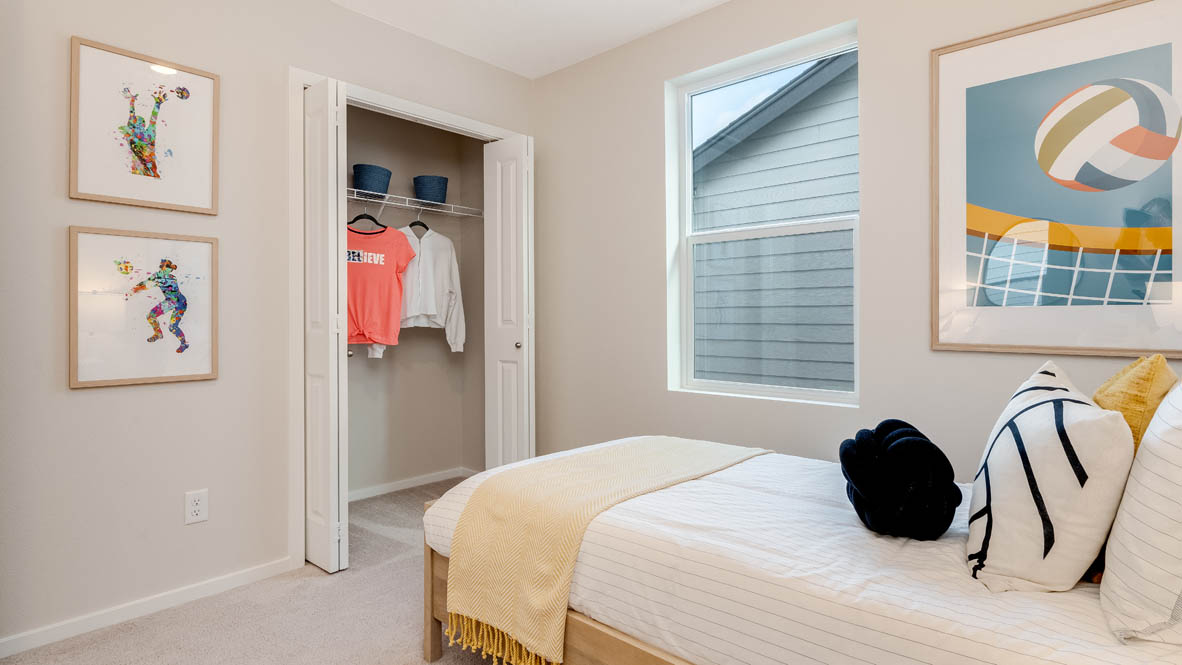 East Park Village Bedroom with a bed with sheets, light stained bed frame, end table with a lamp, paintings, and a window, with a closet