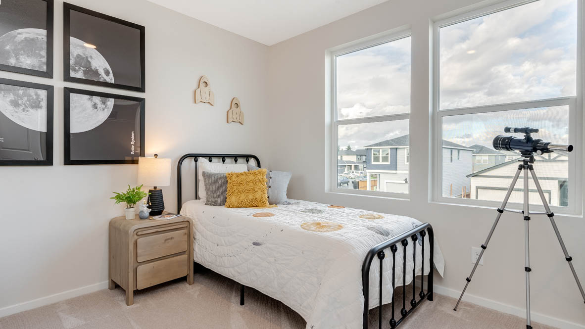East Park Village Bedroom with a bed with sheets, light stained bed frame, end table with a lamp, paintings, and a window, and a telescope