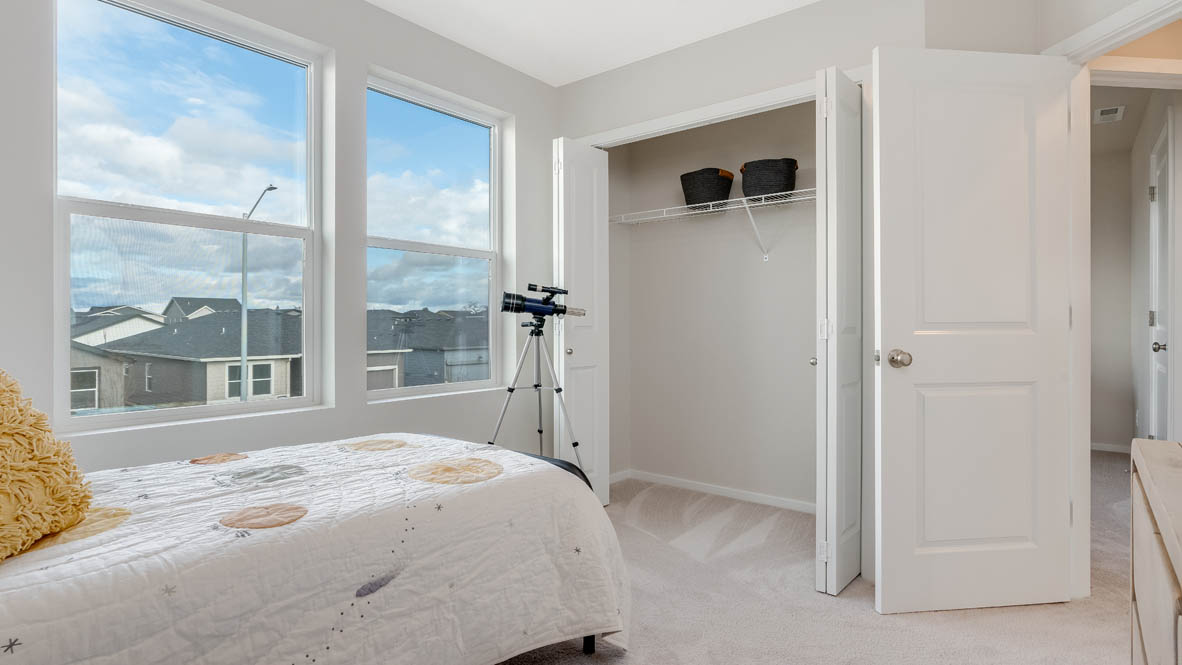 East Park Village Bedroom with a bed with sheets, light stained bed frame, end table with a lamp, paintings, and a window, and a telescope, and a closet