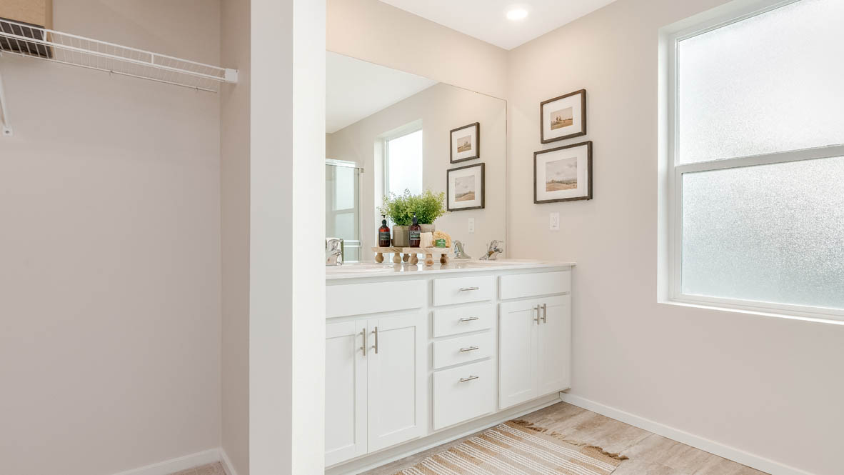 East Park Village Primary bathroom with view of walk in closet, white cabinets, quartz countertops, mirror, and window