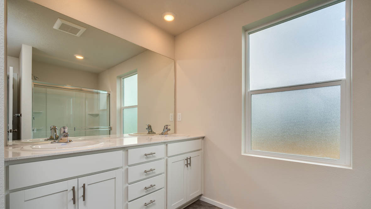 East Park Village bathroom with double sink vanity, mirror, window, and walk in shower
