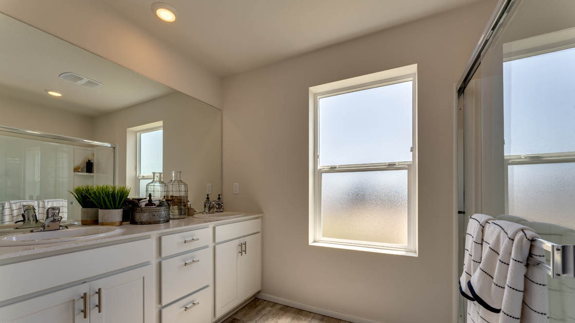 East Park Village bathroom with double sink vanity, mirror, shower, and window