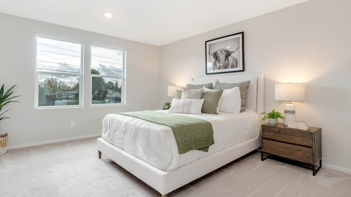 East Park Village Primary bedroom with carpet and a bed with a white bedframe, two end tables, two lamps, pillows, windows, and plants