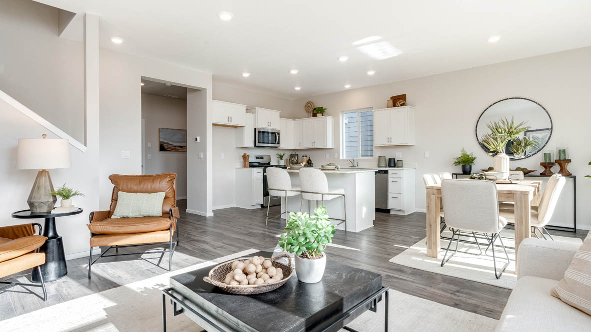 East Park Village great room with laminate flooring, white carpet, a brown chair, entertainment center, white couch, glass coffee table, plants, paintings, and a tv, view of dining room and kitchen