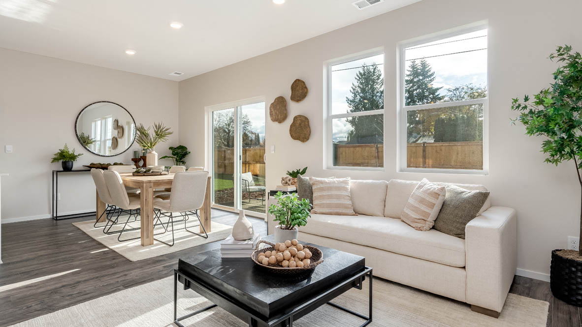 East Park Village great room with laminate flooring, white carpet, coffee table, plants, white couch with pillows, and dining room with a rug and tablet set and chairs