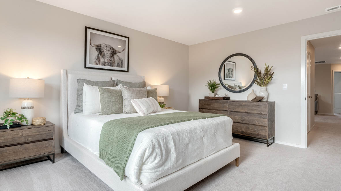 East Park Village Primary bedroom with carpet and a bed with a white bedframe, two end tables, two lamps, pillows, windows, and plants, and console table with a round mirror