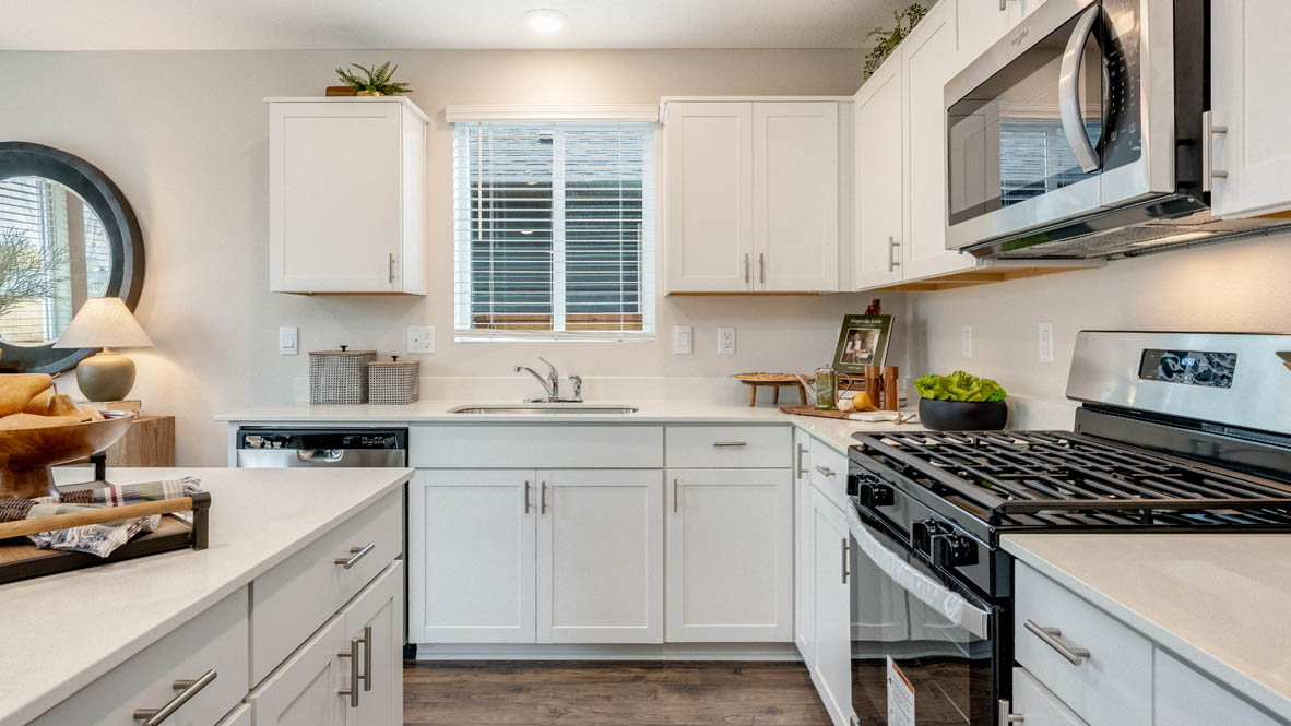 East Park Village kitchen with white quartz countertops, laminate flooring, island with a breakfast bar, shaker style cabinets, windows with blinds, kitchen window, stainless steel appliances