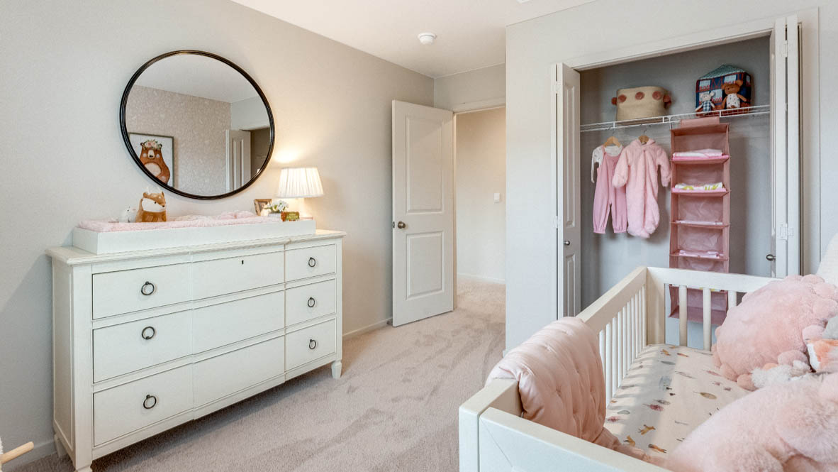 East Park Village bedroom with a white  dresser, circle mirror, painting, pink curtains, carpet, and baby crib